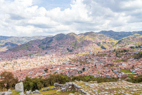 View of the historic city of Cusco nestled in a valley surrounded by mountains, featuring dense urban development with terracotta rooftops and ancient stone ruins in Cusco, Cusco, Peru.