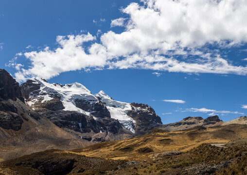 View of the snow-capped peaks of the Andes mountains under a bright blue sky with wispy clouds in the high altitude landscape of Ancash, Peru.
