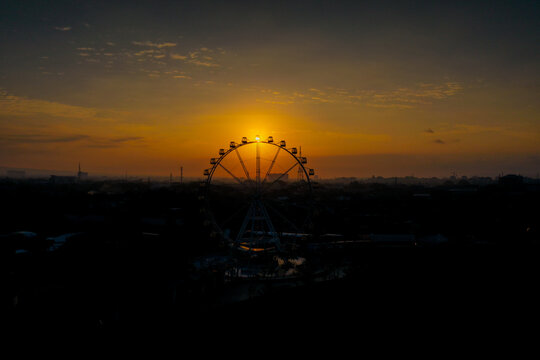 Aerial view of the Ferris wheel at SKE City Park silhouetted against a vibrant golden sunset sky in Kecamatan Mlati, Daerah Istimewa Yogyakarta, Indonesia.