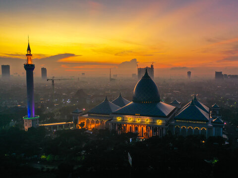Aerial view of al-Akbar National Mosque Surabaya with its large blue dome and minaret illuminated against a vibrant sunset sky in Kecamatan Jambangan, Jawa Timur, Indonesia.