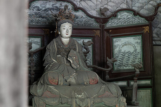 View of the ornate statue of a deity at Jinci Temple, featuring intricate traditional robes and an elaborate headdress set against a painted wooden screen in Taiyuan, Shanxi, China.