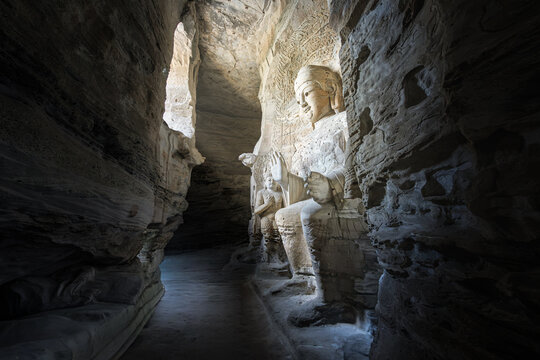View of the ancient stone carved Buddha statues inside the Yungang Grottoes, featuring intricate rock textures and dramatic light filtering into the cave in Datong, Shanxi, China.