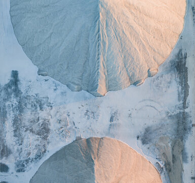 Aerial view of two symmetrical sea salt stockpiles divided by a textured mineral surface, illuminated by soft golden sunset light in France.