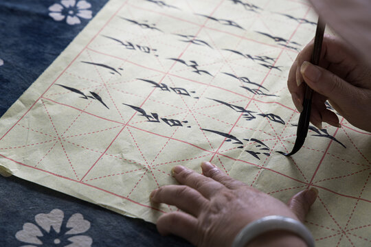 View of a woman practicing Nushu calligraphy with a traditional brush on grid-lined paper in Yongzhou, Hunan, China.