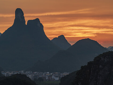 Aerial view of Yangshuo County karst mountains silhouetted against a vibrant orange sunset sky above the town in Guilin, Guangxi, China.