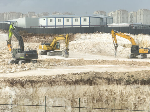 View of three excavators working on a rocky construction site with temporary buildings in the background in Basaksehir, Istanbul, Turkiye.