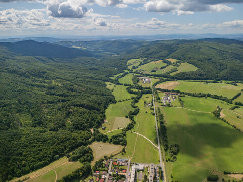 Aerial view of Kokava nad Rimavicou surrounded by rolling green hills, lush forests, and agricultural fields under a blue sky in Kokava nad Rimavicou, Banska Bystrica Regio, Slovakia.