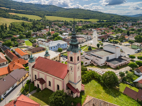 Aerial view of the historic church with a tall steeple and red roof, surrounded by town buildings and green hills in Kokava nad Rimavicou, Banska Bystrica Regio, Slovakia.