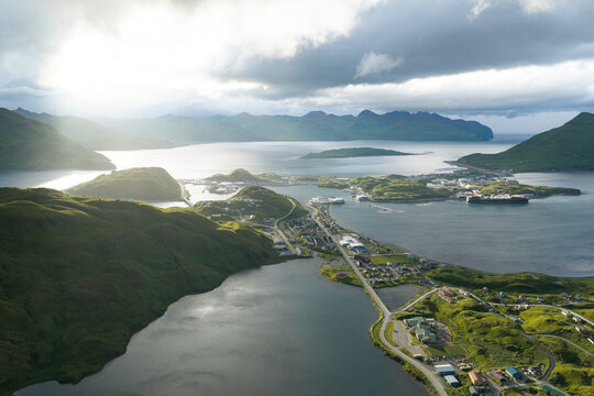 Aerial view of the coastal town of Unalaska nestled among lush green hills and surrounded by the waters of the Bering Sea in Unalaska, Alaska, United States.