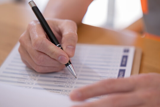 Person completing a questionnaire with pen on paper, representing survey, assessment, feedback, evaluation, checklist, research, data collection and customer satisfaction in a professional setting.