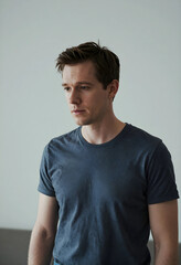 Obraz premium Young adult man with short brown hair and a dark gray t-shirt looking down with a thoughtful expression, headshot portrait