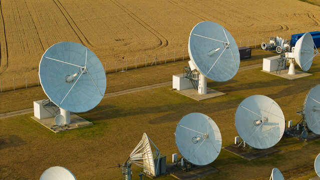 Aerial view of the Satellite Mediaport Services Ltd. facility with large white satellite dishes in a grassy field next to a golden wheat field in Long Lawford, England, United Kingdom.