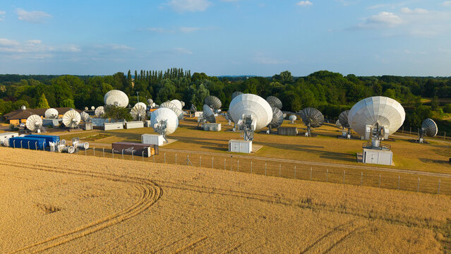 Aerial view of Satellite Mediaport Services Ltd. with large satellite dishes set amidst a golden wheat field and lush trees in Long Lawford, England, United Kingdom.