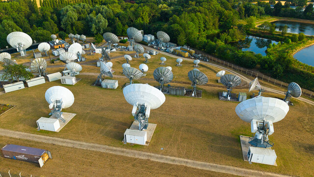 Aerial view of Satellite Mediaport Services Ltd. featuring numerous large satellite dishes in a grassy field with surrounding trees and ponds in Long Lawford, England, United Kingdom.