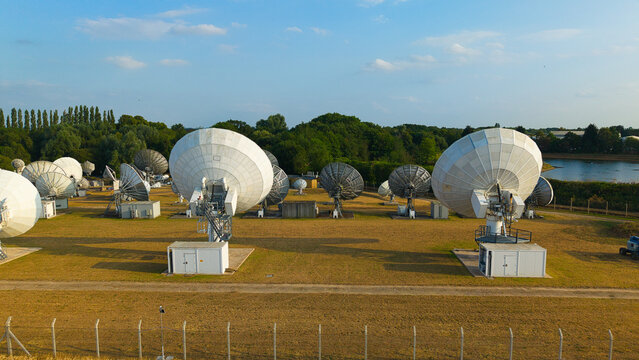 Aerial view of Satellite Mediaport Services Ltd. featuring large communication satellite dishes arranged in a field with surrounding trees and a pond in Long Lawford, England, United Kingdom.