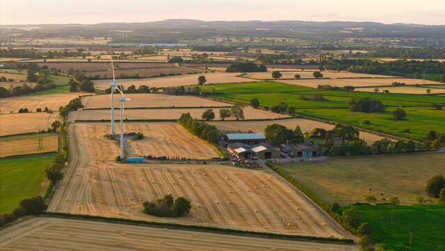 Aerial view of golden harvest fields with wind turbines and farm buildings in the rural landscape of Enderby, England, United Kingdom.