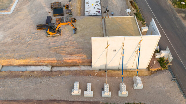 Aerial view of a construction site featuring a concrete wall supported by braces, an excavator, and foundation blocks in Trier-Saarburg, Rhineland-Palatinate, Germany.