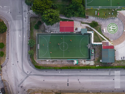 Aerial view of a soccer field with players in orange jerseys during a match, surrounded by paved areas and trees in Avellino, Campania, Italy.
