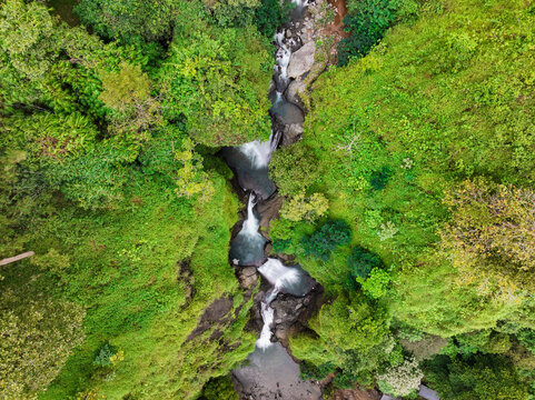 Aerial view of Curug Jagapati waterfall cascading through lush tropical forest and rocky terrain in Cisompet, West Java, Indonesia.