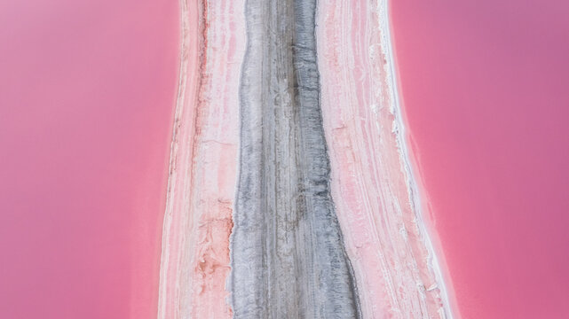 Aerial view of a narrow service road dividing vibrant pink salt ponds in the Camargue, France.