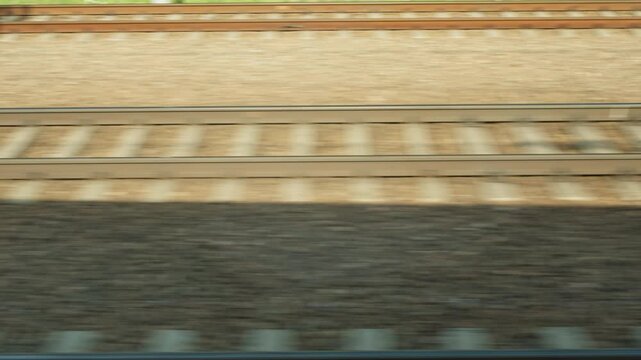 Railroad tracks blur past during a high speed train trip. Steel rails and wooden sleepers lie on gravel ballast. Fast rail transport symbolizes travel, journey, logistics and connectivity.