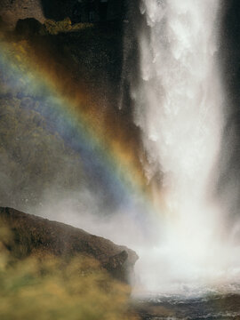 View of Kvernufoss waterfall cascading over rocky cliffs with a vibrant rainbow appearing in the mist in Evindarholar, Rangarthing eystra, Iceland.