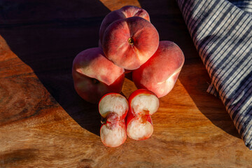 Freshly picked flat peaches with one cut open, showing juicy white flesh on a rustic wooden table under natural light © JOSEANTONA