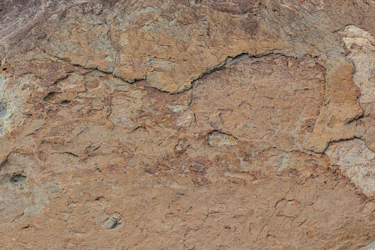 Verwitterte Sandsteintextur mit Rissen und Farbschattierungen, Nahaufnahme einer Felsoberflaeche, natuerliches Hintergrundmuster in Braun- und Ockertoenen