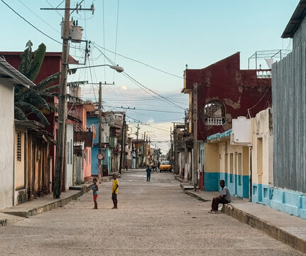Cuba - 20 December 2024: View of a quiet street in Cuba with colorful buildings, overhead power lines, and local residents standing and sitting along the sidewalk.
