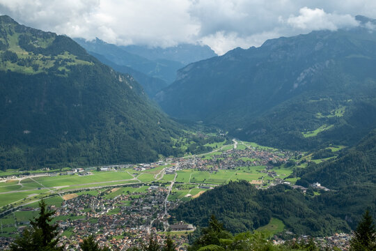 View of Interlaken nestled in a lush green valley surrounded by towering mountains under a cloudy sky in the Bernese Oberland region, Interlaken, Canton of Bern, Switzerland.