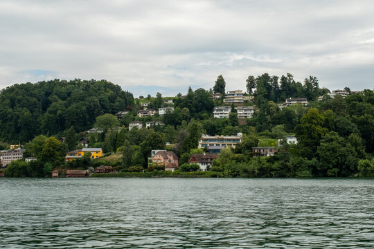 View of residential houses nestled on a lush green hillside overlooking the calm waters of Lake Lucerne in Lucerne, Lucerne, Switzerland.