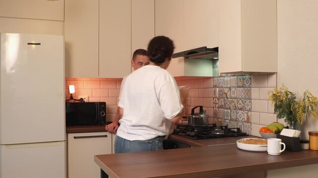 Happy young partners sharing laughter and conversation in a stylish kitchen. Their relaxed body language reflects emotional intimacy, mutual respect, and a positive home lifestyle. Wide shot