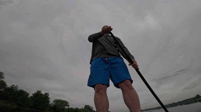 Man paddling SUP on cloudy lake