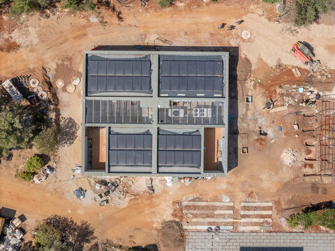 Aerial view of a building under construction featuring solar panels on the roof, surrounded by dirt ground and construction equipment in Cascais, Lisboa, Portugal.