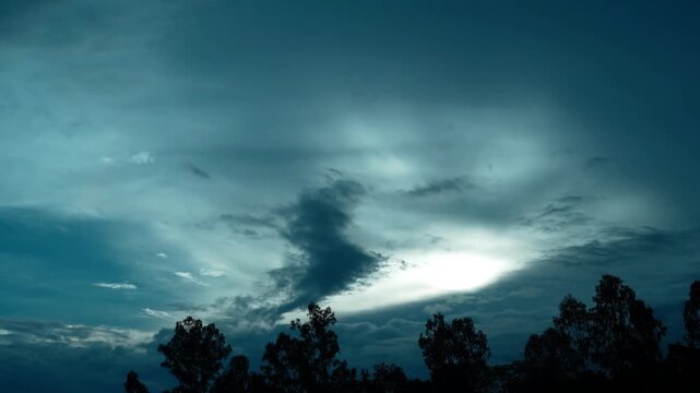 Silhouette of green trees under a dramatic blue sky with soft glowing clouds