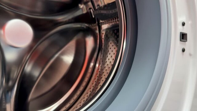 Close-up steel drum washing machine door showing gleaming stainless interior with perforated pattern, open rubber gasket, visible.