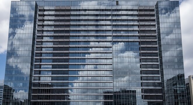 Modern glass office building facade reflecting blue sky and clouds