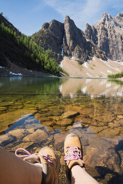 View of hiking boots submerged in the clear, rocky waters of Lake Louise with the majestic Rocky Mountains in the background in Lake Louise, Alberta, Canada.