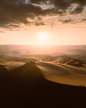 Aerial view of the sand dunes of Huacachina at sunset with people standing on the ridge under a dramatic golden sky in Huacachina, Ica, Peru.