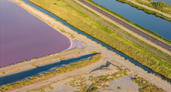 Aerial view of pink salt evaporation ponds in the Camargue region, featuring industrial salt production basins, adjacent canals, and surrounding wetlands in France.