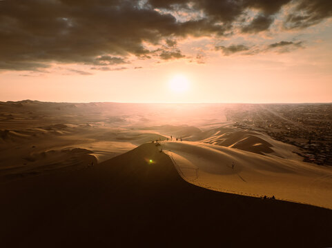 Aerial view of Huacachina oasis surrounded by vast sand dunes under a golden sunset sky in Huacachina, Ica, Peru.