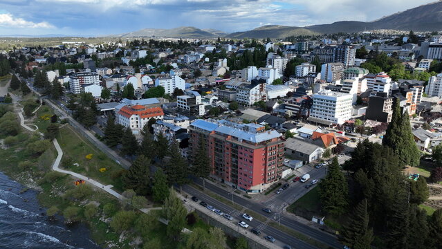 Aerial view of the urban landscape featuring dense residential buildings, evergreen trees, and the waterfront along the lake in San Carlos de Bariloche, Rio Negro, Argentina.
