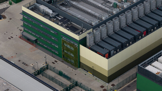 Aerial view of the NTT LON1B Data Centre featuring large cooling units on the roof, a green wall facade, and surrounding industrial infrastructure in Dagenham, England, United Kingdom.