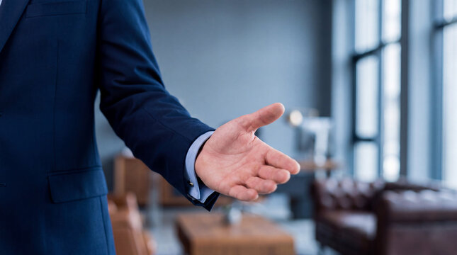 Professional businessman in a navy suit extends his hand for a firm handshake.