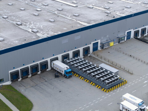 Aerial view of a modern logistics hub featuring multiple loading docks, parked semi-trucks, and industrial cooling units in the paved yard in Skawina, Lesser Poland Voivode, Poland.