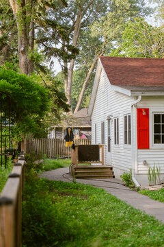 View of a white cottage with red shutters nestled among lush trees and greenery on the Toronto Islands in Toronto, Ontario, Canada.
