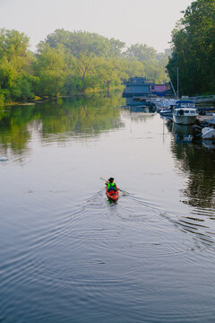 View of a person kayaking on a calm channel at Toronto Islands with docked boats and lush green trees in the background in Toronto, Ontario, Canada.