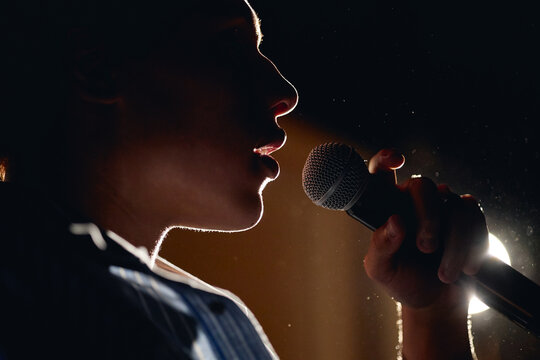 Silhouette of teenager singing into microphone on stage during student theater performance. Image represents youth arts education and is suitable for drama school promotion, close up