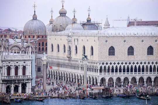 Aerial view of St. Mark's Basilica and the Doge's Palace with crowds of people in the square and gondolas moored along the waterfront in Venice, Veneto, Italy.