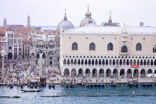 Aerial view of the Doge's Palace and St. Mark's Square featuring historic architecture, gondolas moored along the waterfront, and crowds of people in Venice, Veneto, Italy.